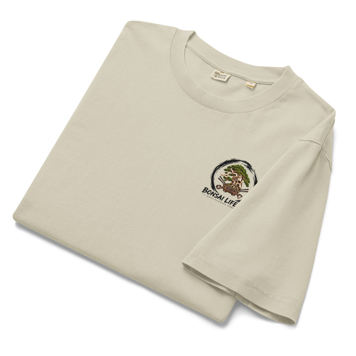 Folded stone beige T-shirt showing small circular bonsai pirate skull chest emblem