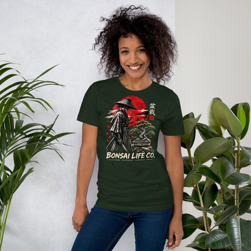 Model wearing heathered dark green T-shirt with samurai beside a green bonsai and red sun with Bonsai Life Co. lettering, beside leafy plants