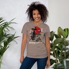 Model wearing taupe T-shirt with samurai beside a green bonsai and red sun with Bonsai Life Co. lettering, beside leafy plants