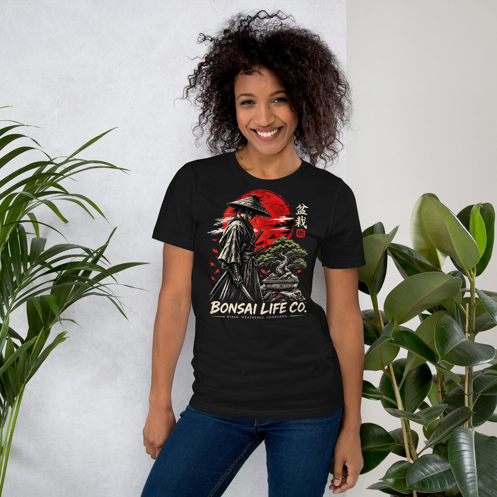 Model wearing vintage black T-shirt with samurai beside a green bonsai and red sun with Bonsai Life Co. lettering, beside leafy plants