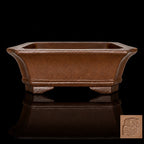 Brown rectangular bonsai pot on a reflective black surface, with an inset showing its impressed seal