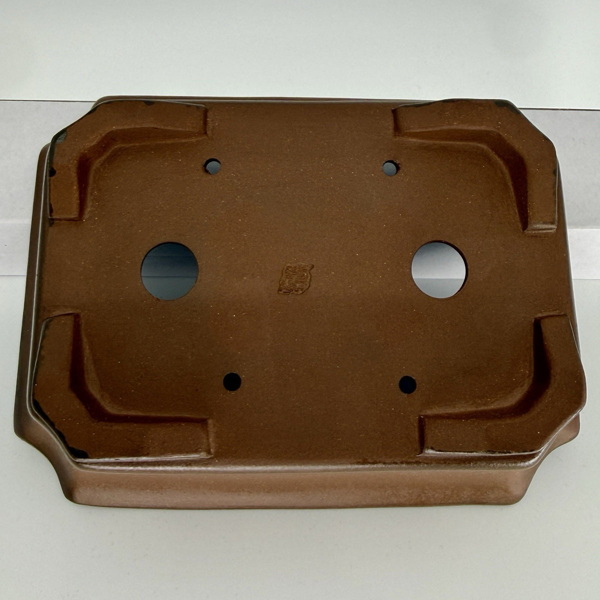 Close underside view of the brown pot with two drainage holes and four smaller tie-down openings